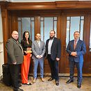 Five people in front of a door. One of these people holds an award in her hand.